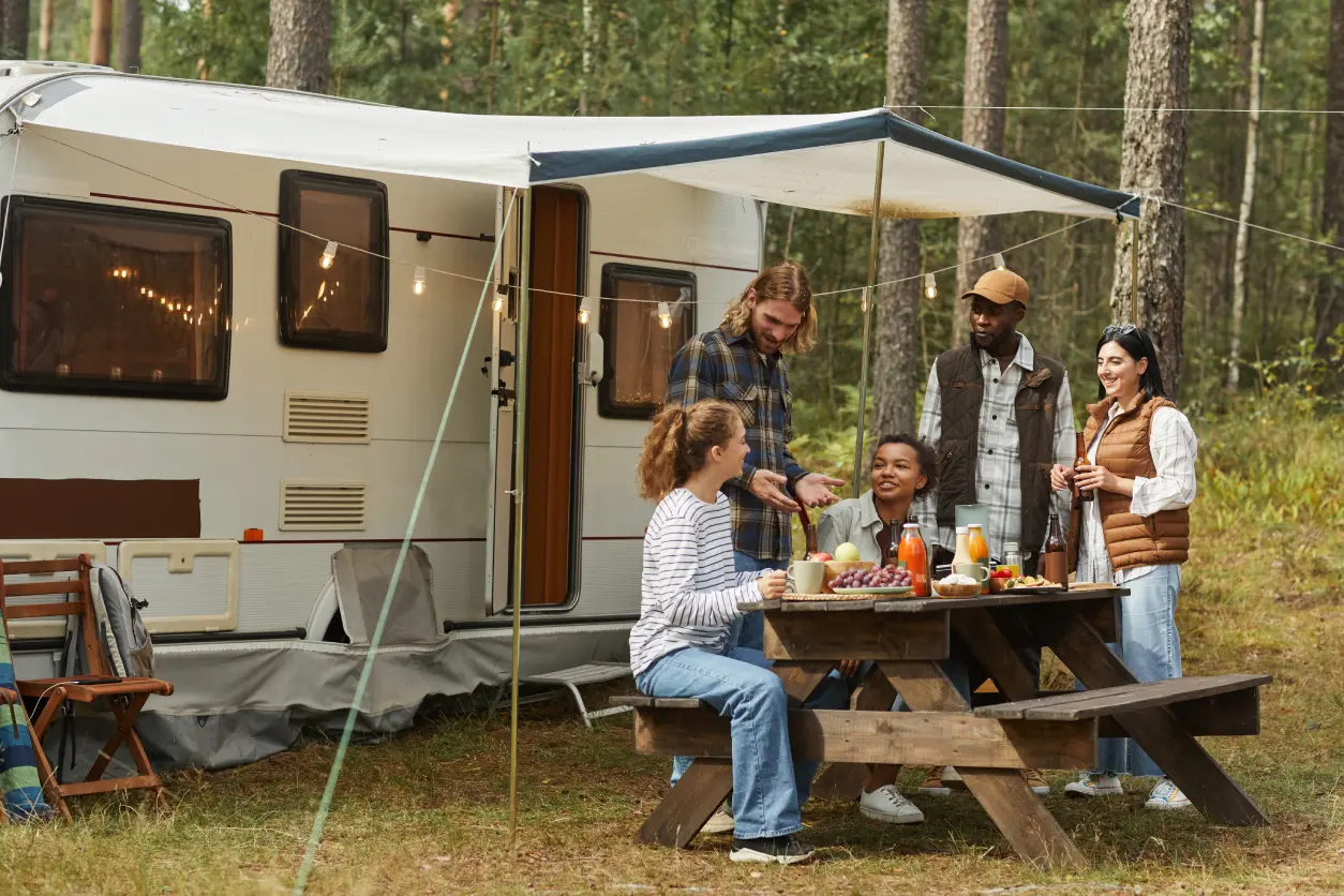 New Project(8) Group enjoying picnic by camper in forest.